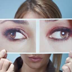 Eine Frau hält zwei Fotos von Augen vor ihr Gesicht. 