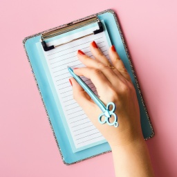 Nahaufnahme einer Hand, die mit einem Stift auf einem Notizzettel liegt.