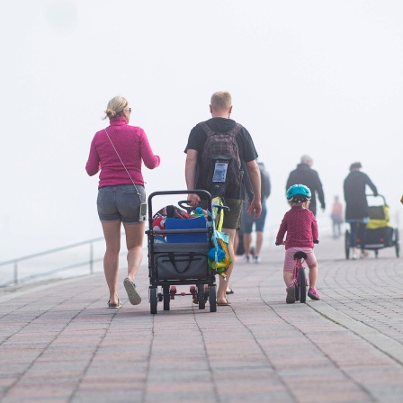 Eine Familie spaziert auf dem Deich entlang, links von ihnen liegt das Meer.