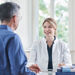 Lächelnde Ärztin sitzt mit einem männlichen Patienten am Tisch