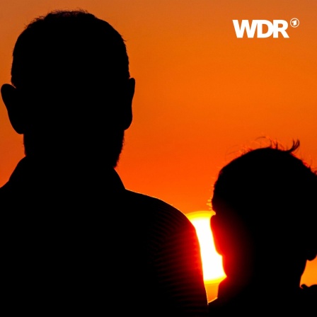 Vater und Sohn stehen mit dem Rücken zur Kamera vor einem Sonnenuntergang.