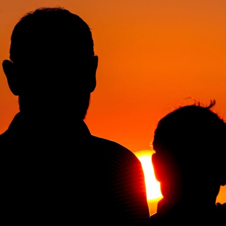 Vater und Sohn stehen mit dem Rücken zur Kamera vor einem Sonnenuntergang.