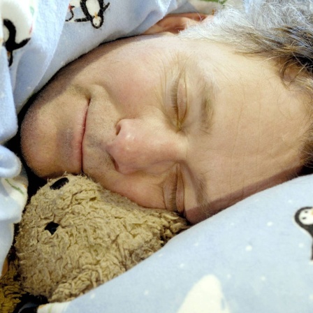 Mann schläft mit Teddy in Kinderbettwäsche