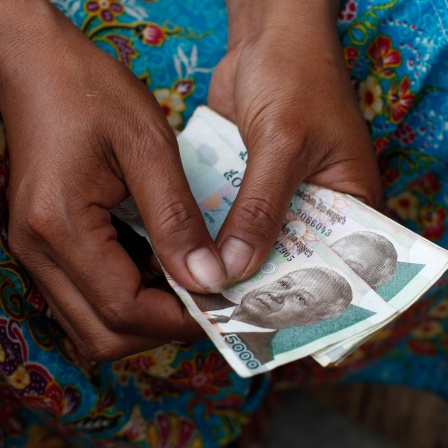 Weibliche Hände mit dunkler Hautfarbe halten ein Bündel kambodschanische Geldscheine