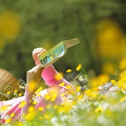 Eine Frau liest auf einer gelben Blumenwiese ein Buch.