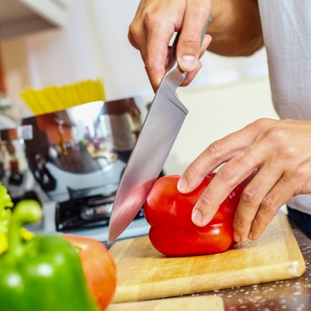 Ein Mann schneidet eine Paprika auf einem Holzbrett. 