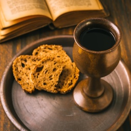Brot, Wein und eine Bibel liegen auf einem Holztisch.