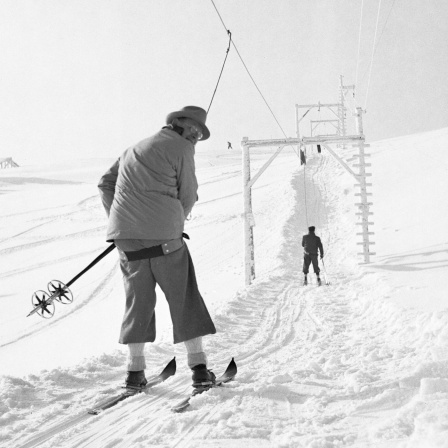 Ein Skifahrer fährt mit dem Skilift den Hang hinauf