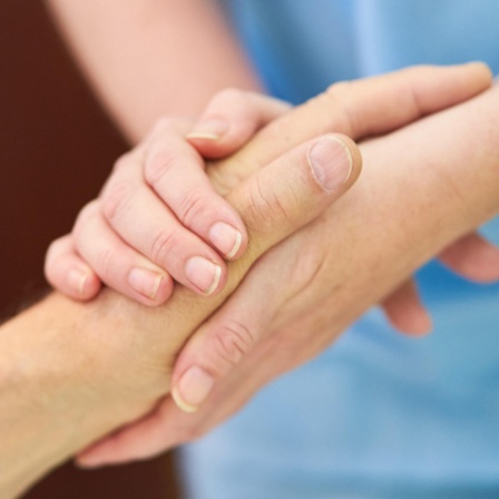 Eine Pflegekraft hält die Hände eines Patienten.