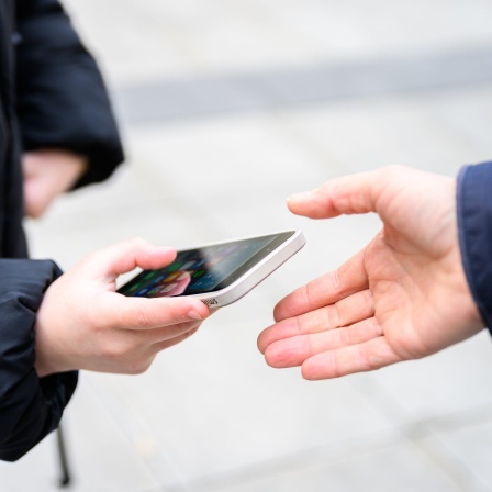 Schüler reicht einem Lehrer sein Handy