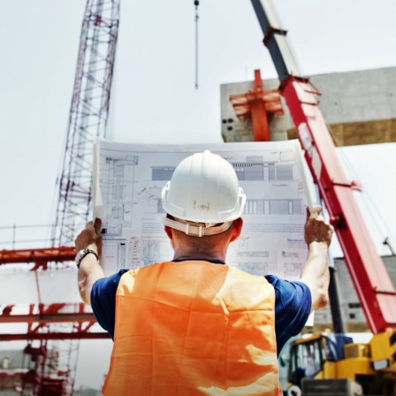 Ein Bauarbeiter schaut sich einen Bauplan auf einer Baustelle an.