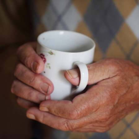 Ein älterer Mann hält eine wärmende Tasse Tee in den vom Alter gezeichneten Händen.