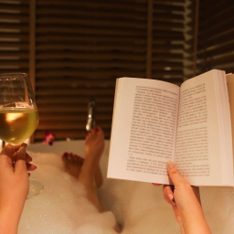 Junge Frau mit Wein und Buch in der Badewanne