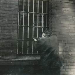 Mann hält Waffe aus einem vergitterten Fenster
