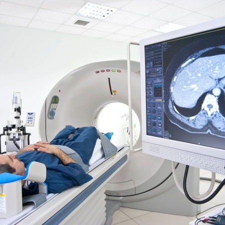 Mann auf einer Liege eines Scanners, auf der Seite Bildschirm mit Querschnitt eines Körpers