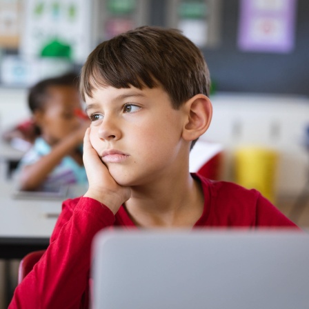 Ein Junge sitzt traurig in seiner Schulklasse und schaut abwesend in die Ferne. Zu oft werden Signale der Gewalt an Kindern nicht erkannt - auch nicht von jenen, die in Kitas, Schulen, Arztpraxen und Jugendämtern mit ihnen zu tun haben.