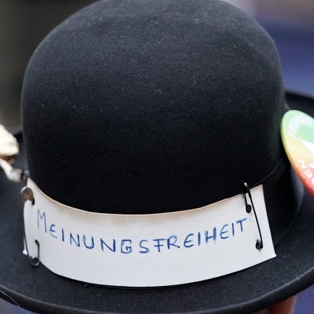 Schwarzer Hut, an dem mit Stecknadeln ein Zettel mit der Aufschrift "Meinungsfreiheit" befestigt ist.