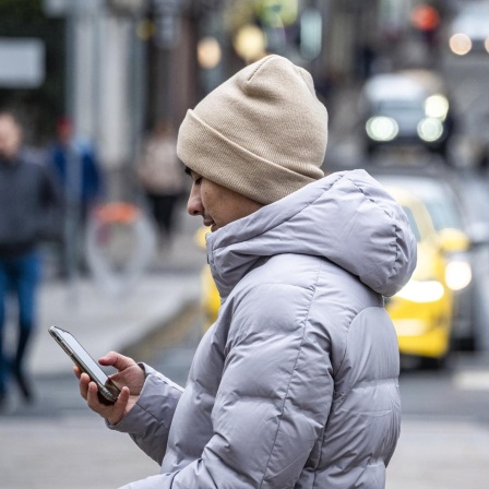 Ein Jugendlicher überquert eine Straße und schaut dabei auf sein Smartphone.