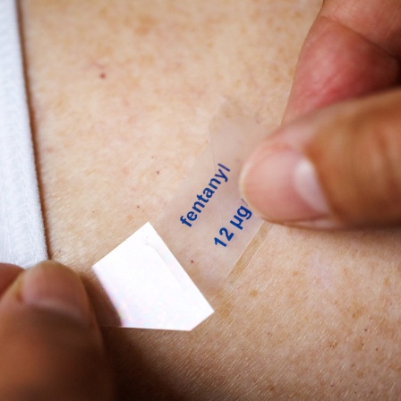 Eine Frau drückt einer Dame ein Fentanylpflaster mit der Aufschrift fentanyl 12 Mikrogramm pro Stunde auf den Rücken.