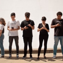 Junge Menschen stehen nebeneinander und schauen alle in ein Smartphone.