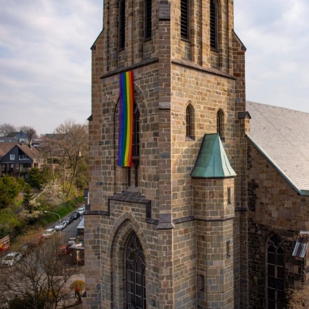 Eine Regenbogenfahne hängt an einem Kirchturm
