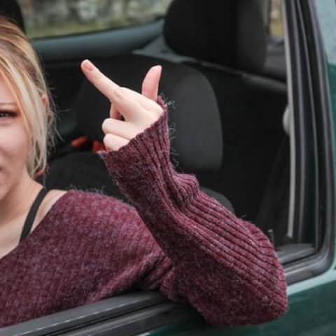 Junge blonde Frau zeigt anderen Autofahrern den Stinkefinger und droht.