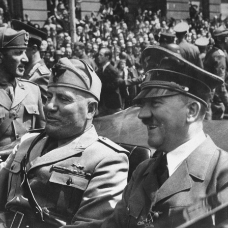 Schwarz-weiss Bild von Adolf  Hitler  (R)  und  Benito  Mussolini  bei einer Fahrt im Cabrio. Im Hintergrund viele Menschen.