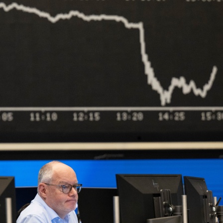 Ein Aktienhändler an der Börse schaut vor der Dax-Kurve auf einen Bildschirm.