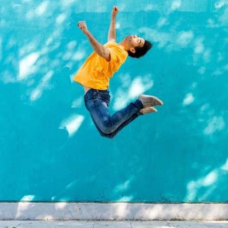 Mann springt vor blauer Wand hoch in die Luft. Was ist Schwerkraft?