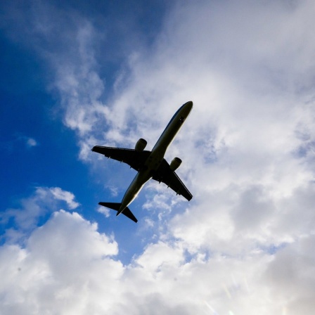 Ein Flugzeug in der Luft unter blauem Himmel mit ein paar Wolken.
