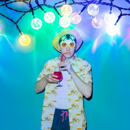 Ein Mann, der einen Cocktail trinkt steht unter einer Party-Lichterkette.