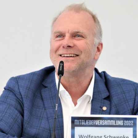 Wolfgang Schwenke, der Geschäftsführer von Holstein Kiel, sitzt bei einer Pressekonferenz hinter einem Mikrofon und lacht.