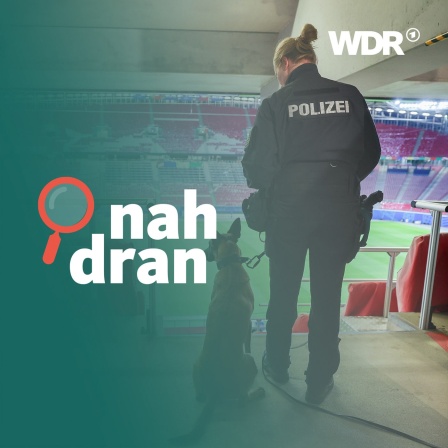 Eine Polizistin steht mit einem Diensthund in einem leeren Fußballstadion und schaut auf die Tribünen 