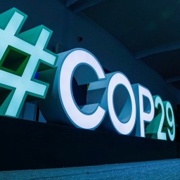 Ein blau und grün beleuchteter dreidimensionaler Schriftzug zeigt den Hashtag COP29