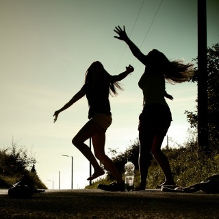 Zwei junge Frauen tanzen wild auf der Straße und fühlen sich gut dabei.