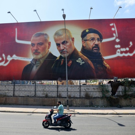 An einer Straße steht ein Banner mit Porträts der getöteten Milizenführer Ismail Haniyeh, Qasem Soleimani und Fuad Shukr.