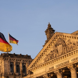 Zwei Deutschland-Flaggen wehen vor und auf dem Reichstagsgebäude bei Sonnenuntergang. Auf dem Giebel ist die Inschrift «Dem Deutschen Volke» zu lesen.