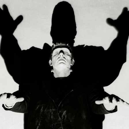 Frankenstein's Monster hebt bedrohlich die Arme, sein Schatten lässt ihn noch größer wirken.
