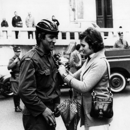 Schwarzweißfoto: Eine Frau heftet am 25.04.1974 einem Soldaten in Lissabon, Portugal, eine rote Nelke an. Die rote Nelke ist das Symbol der portugiesischen Revolution.