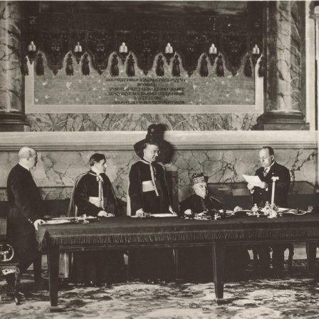 Vertragsunterzeichnung im Lateranspalast am 11. Februar 1929 mit Kardinalstaatssekretär Pietro Gasparri und dem faschistischen Ministerpräsidenten Italiens Benito Mussolini am Mikrofon stehend.