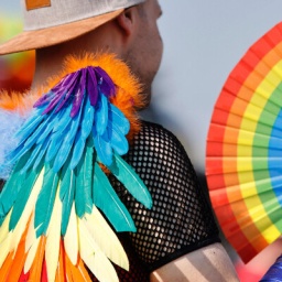 Ein Teilnehmer bei der Parade des Christopher Street Day 2023 in Köln. Er hält einen Fächer in Regenbogenfahnen in der Hand.
