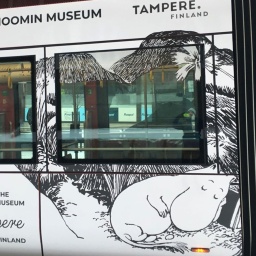 Eine weiße Strahenbahn steht an einer Haltestelle, darauf abgebildet sind schlafende Mumins (Comiczeichnungen mit rundlichen Fabel-Tieren aus Finnland)