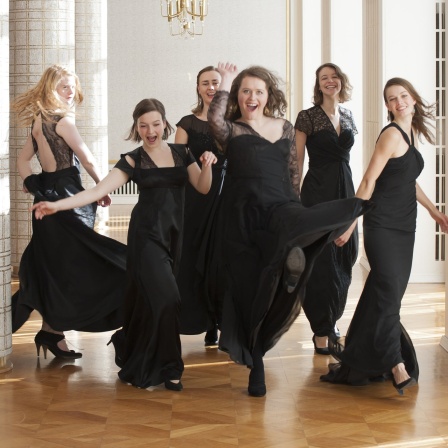 Das Ensemble Sjaella in einem Gang. Junge Frauen mit schwarzem, langen Kleid, dynamisch (springend, drehend)