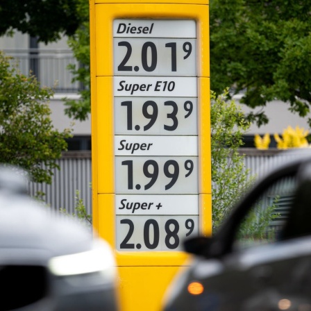 Die Preise für Kraftstoffe sind auf der Anzeige einer Tankstelle zu sehen, davor fahren Autos vorbei.