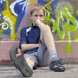 Lustloser neunjähriger Junge sitzt am Boden auf einem Bolzplatz