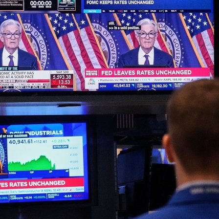 Börse in New York. Mann sitzt vor Bildschirm, auf dem Fed-Chef Jerome Powell zu sehen ist.