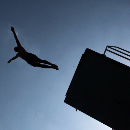 Mann springt vom Zehnmeterturm im Freibad, nur schwarze Silhouette zu sehen