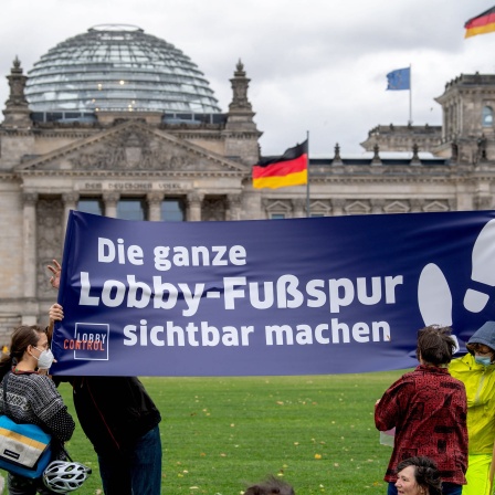Aktivisten zeigen ein Banner des Vereins LobbyControl auf dem Platz der Republik vor dem Reichstagsgebäude mit der Aufschrift: &#034;Die ganze Lobby-Fußspur sichtbar machen&#034;.
