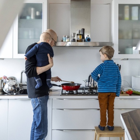 Ein Vater kocht mit seinen Kindern in der Küche, während der Junge mithilft.