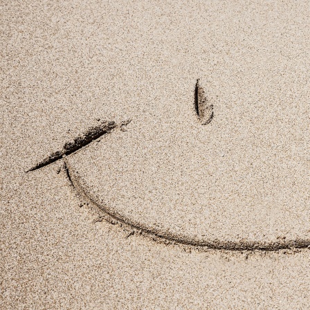 Ein Smiley ist am Strand im Sand gezeichnet.